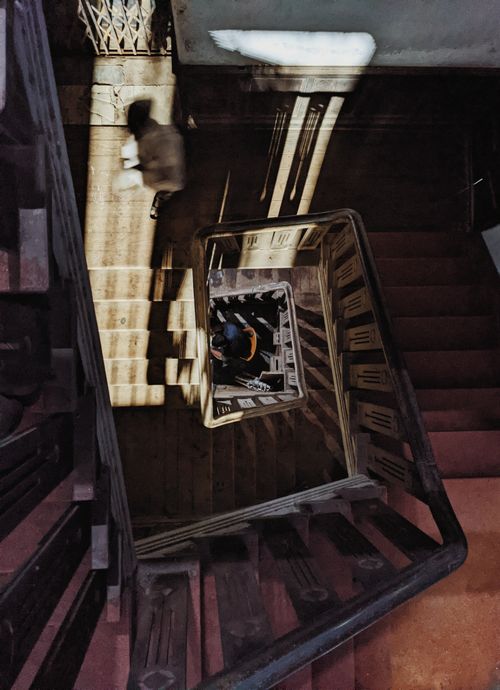 Free Top-down view of a vintage staircase with wooden railing featuring dynamic shadows and abstract patterns. Stock Photo