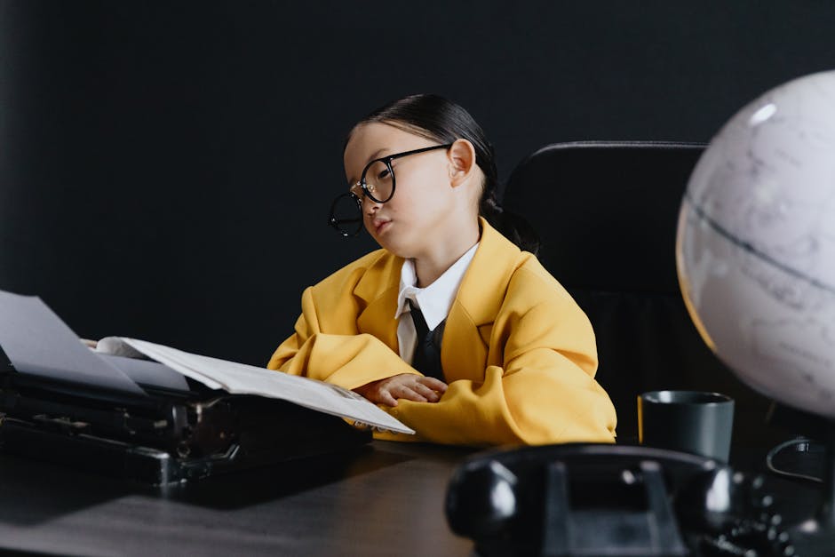 Young girl in oversized suit reading papers at desk with globe and phone.