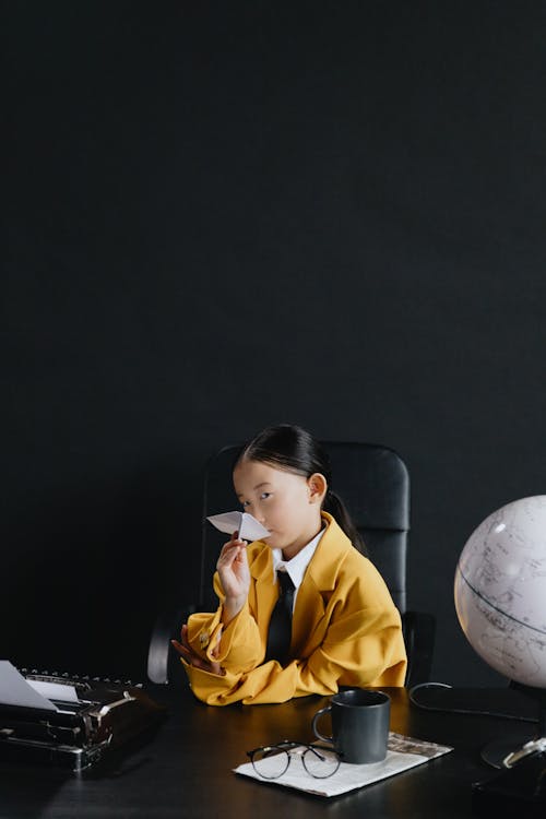 Asian girl in yellow suit sitting and holding plane made from paper