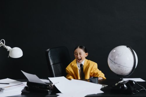 Free Adorable child in yellow suit laughing at office desk with globe and papers. Stock Photo