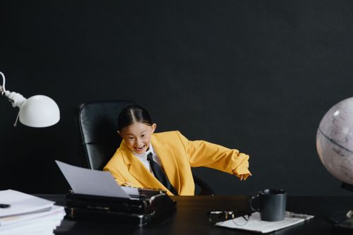 Free Happy child in a yellow jacket at a typewriter, surrounded by office items and a globe. Stock Photo