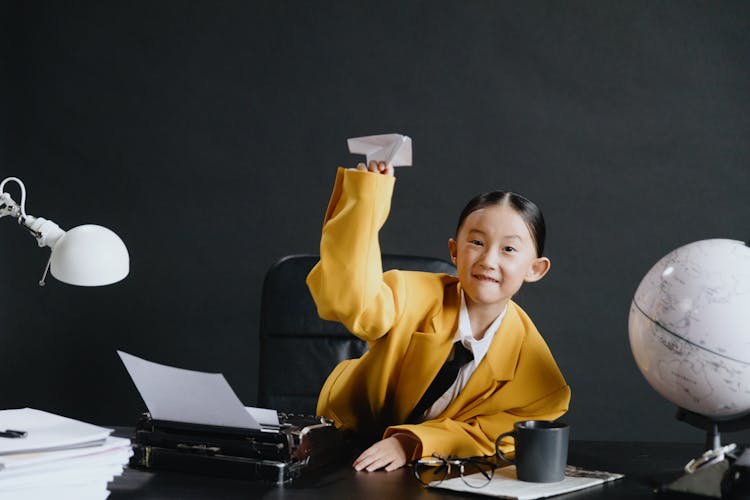 Asian Girl In Yellow Suit Holding Paper-made Plane In Hand