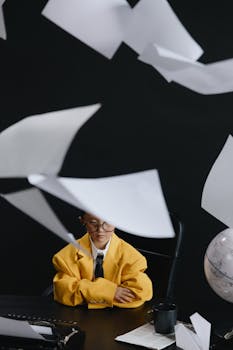 Artistic photo of a child in a yellow suit surrounded by flying papers, creating a whimsical indoor scene.