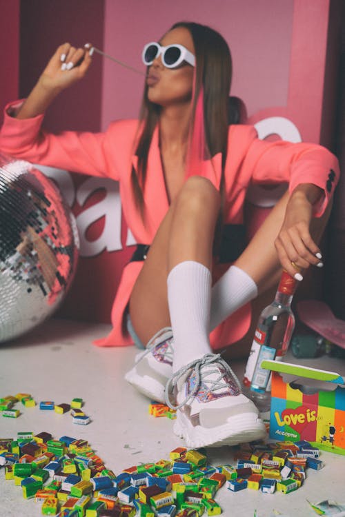 Woman Wearing Sunglasses Sitting Surrounded by Candies and Vodka Bottle