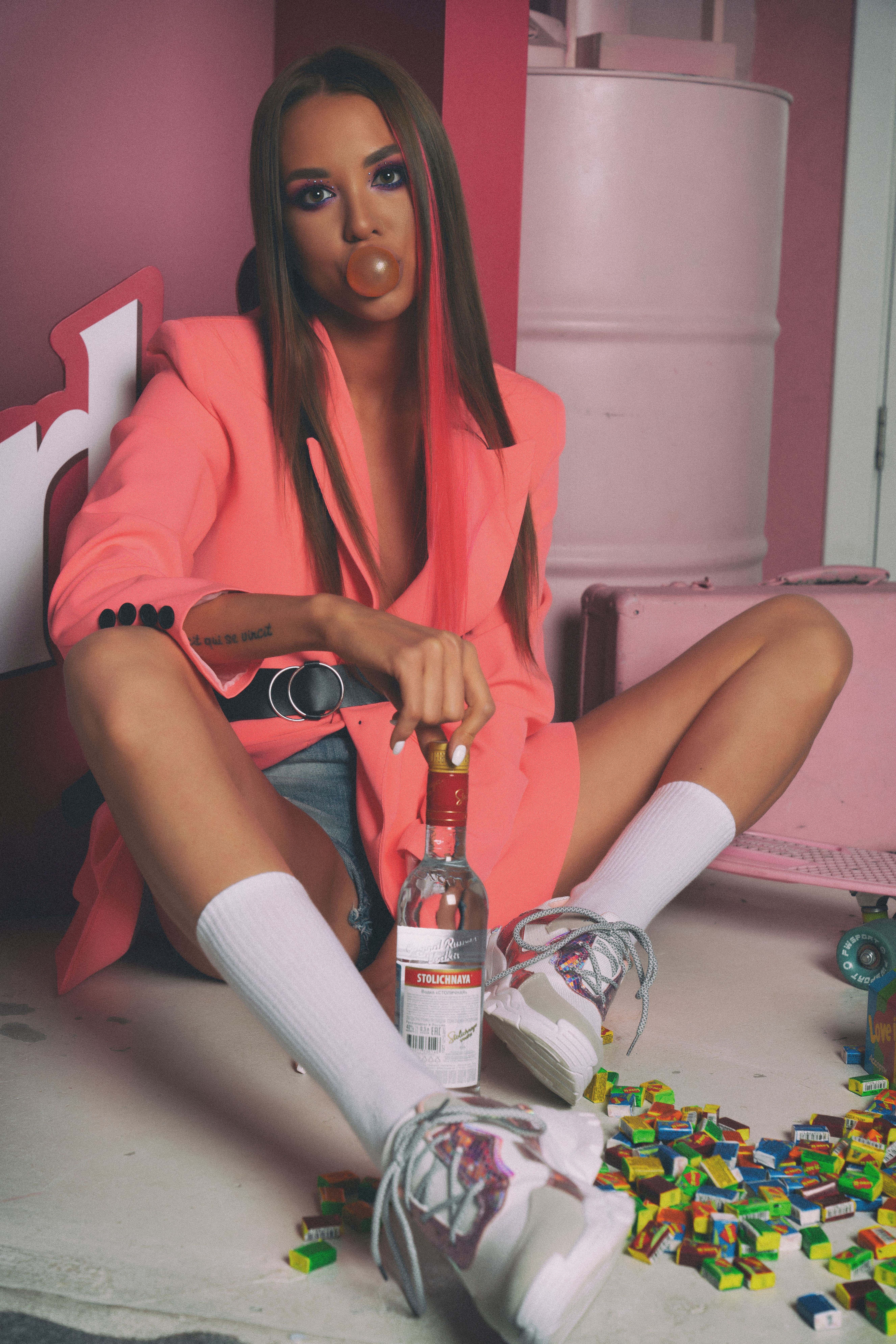 A fashionable young woman in a pink blazer poses with bubblegum indoors, showcasing style and attitude.