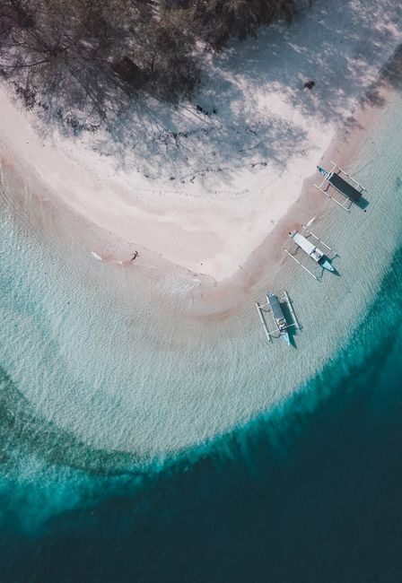 Aerial view of boats anchored on a serene sandy beach with turquoise waters and lush trees.