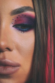 Intense eye makeup with purple and red tones, accented with rhinestones for a dramatic effect.