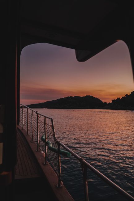 Serene boat deck view at sunset overlooking calm ocean waters and distant islands.