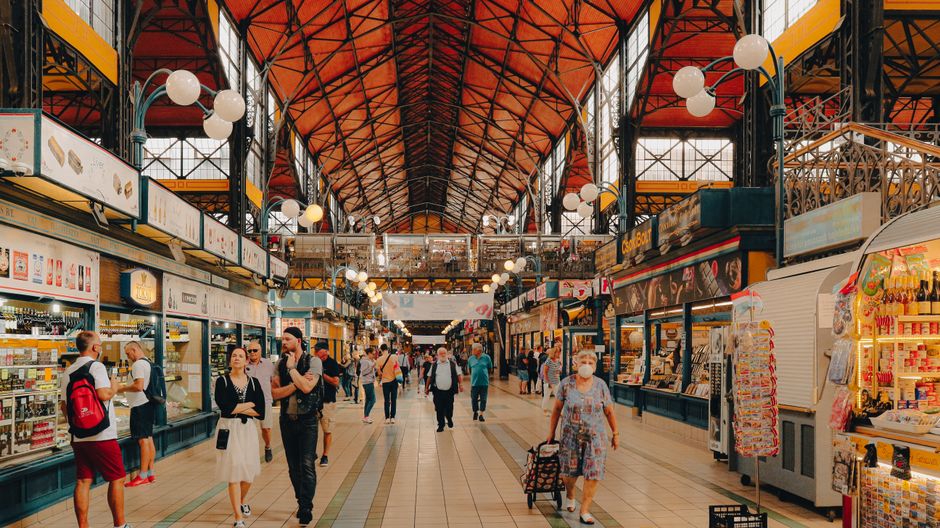 Vista interior de um moderno food hall com iluminação quente e clientes caminhando entre barracas de comida