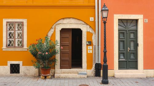 Free Vibrant building facade featuring orange and red walls with distinct doors and a potted plant. Stock Photo