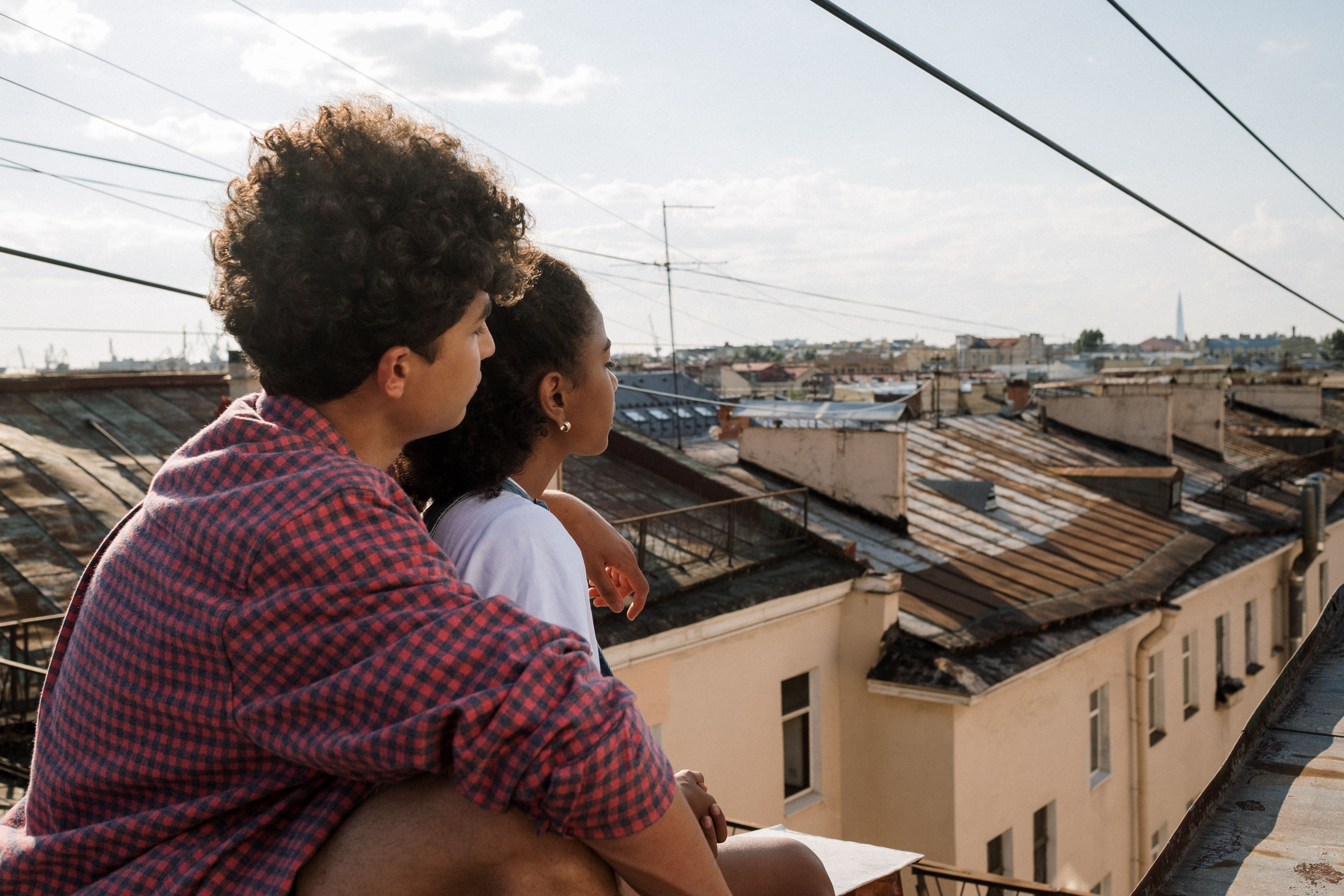 Teenage couple sitting on a rooftop, embracing and looking at the city view, symbolizing love and togetherness.