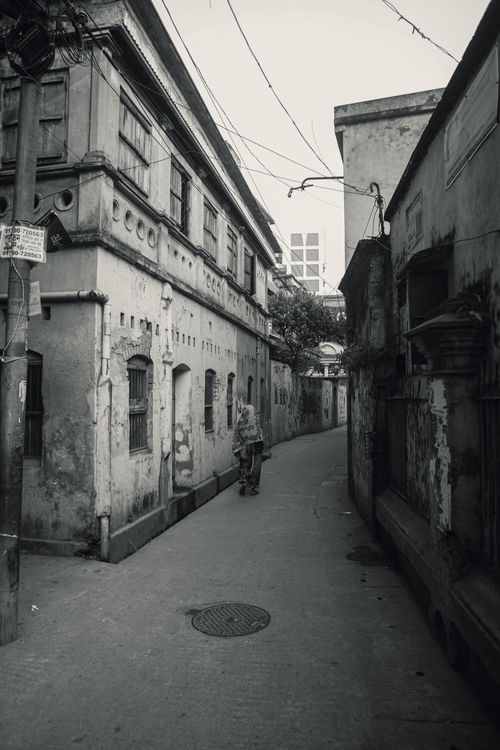 Free Grayscale image of a narrow alley with a solitary figure walking among vintage buildings, exuding a sense of nostalgia. Stock Photo