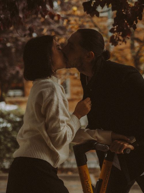 Free A couple shares a romantic kiss under autumn foliage, highlighting affection and intimacy. Stock Photo