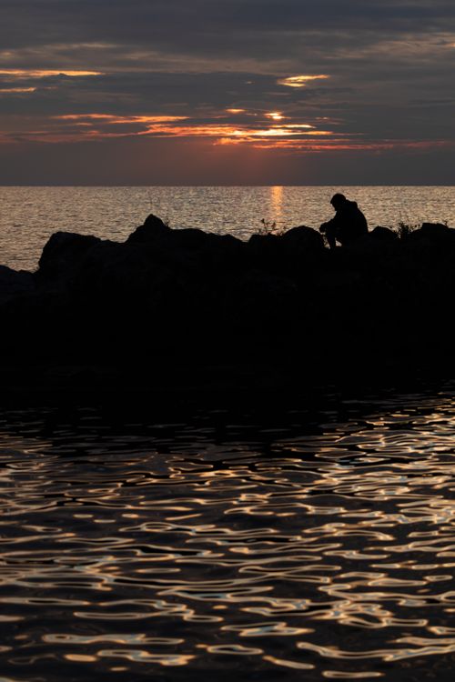 Free Captivating sunset at Montreux seashore with a silhouetted figure sitting on rocks, reflecting over water. Stock Photo