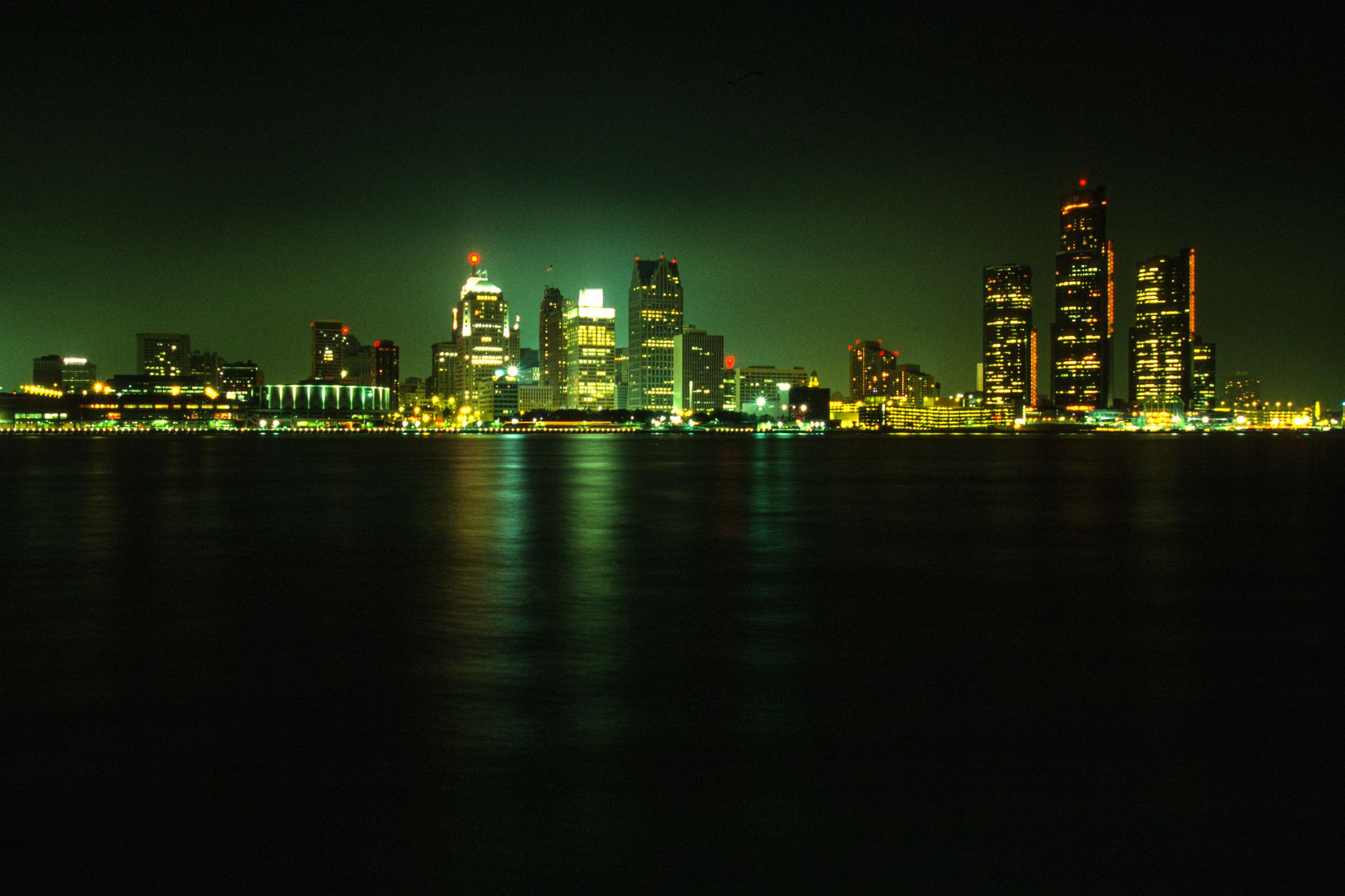 Stunning nighttime view of Detroit's illuminated skyline across a calm river under a dark sky.