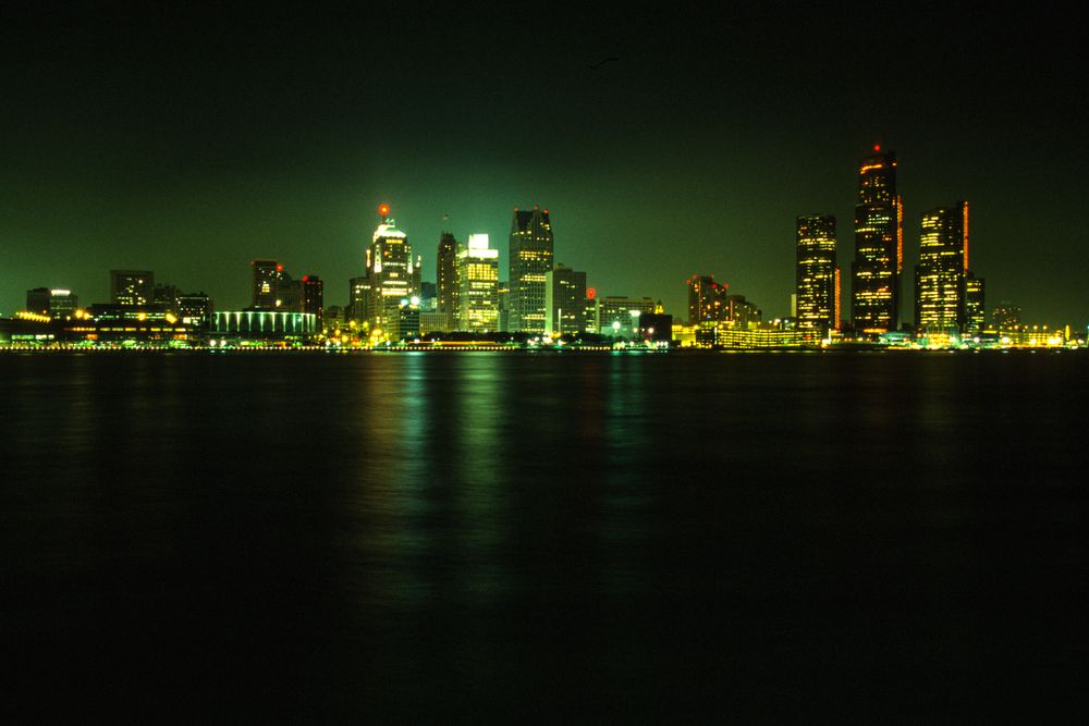 Stunning nighttime view of Detroit's illuminated skyline across a calm river under a dark sky.