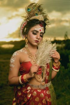 A woman in traditional Indian clothing poses outdoors with intricate jewelry and makeup.