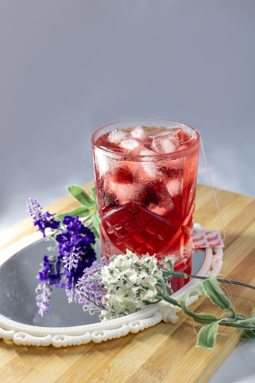 Free Red drink with ice cubes on a vintage mirror surrounded by purple and white flowers. Stock Photo