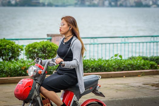 在越南河内，一名年轻女子骑着摩托车，沿着风景优美的泰湖湖畔行驶