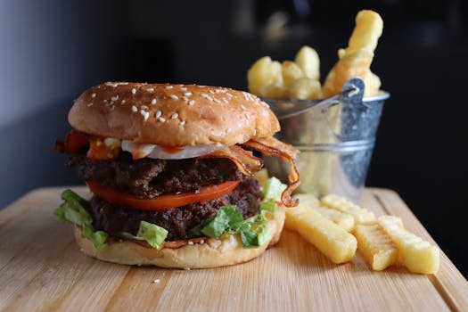 Mouthwatering burger with bacon, tomatoes, and fries on a wooden board.