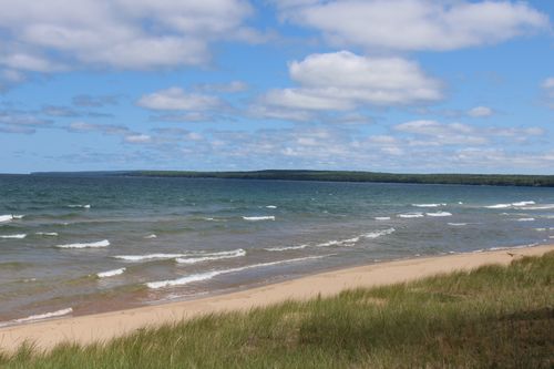 Free Peaceful coastal scene with a sandy beach, gentle waves, and a bright blue sky with clouds. Stock Photo