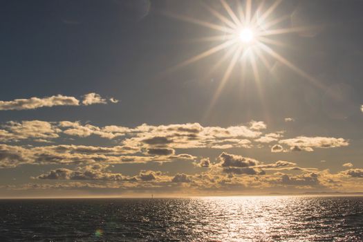 Stunning ocean view with bright sun rays and scattered clouds during a clear day.