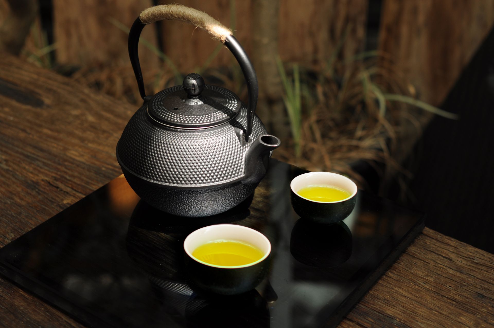 A close-up view of a traditional black teapot with green tea cups on a rustic table, creating a serene scene.