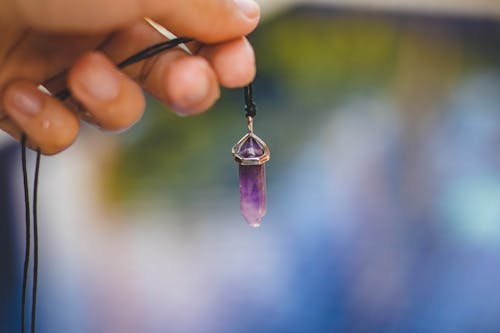 Person Holding Black Necklace With Purple Stone Pendant