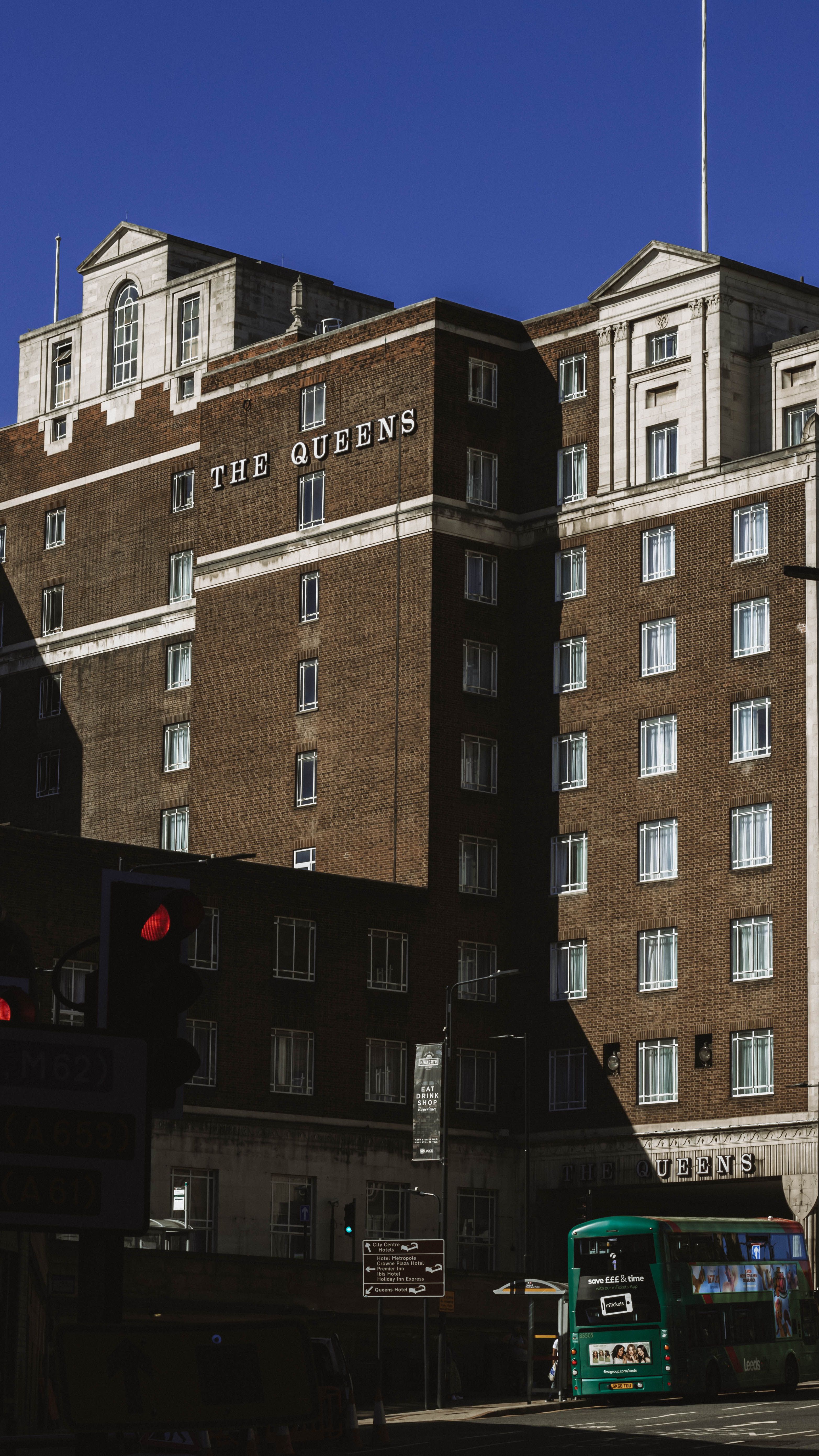 A vibrant street view featuring The Queens Hotel in Leeds, UK, under a clear blue sky.