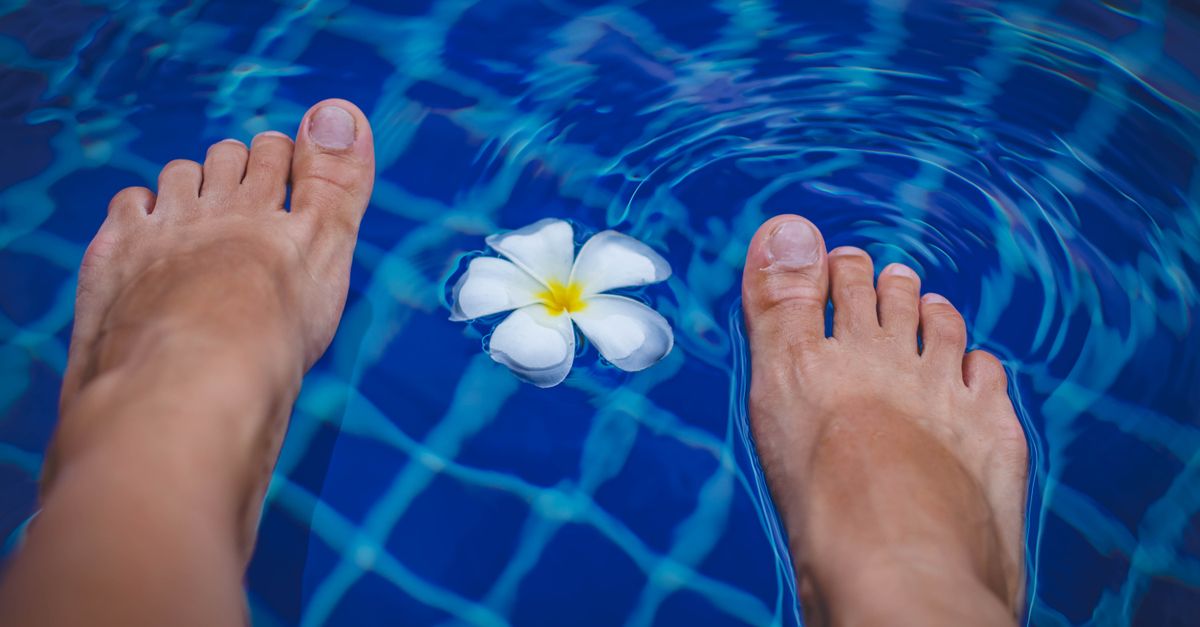 Close-up of feet in a clear blue swimming pool with a floating tropical flower.