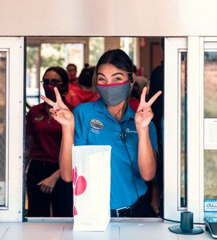Drive-through employee wearing mask flashes a cheerful V sign gesture to customer.