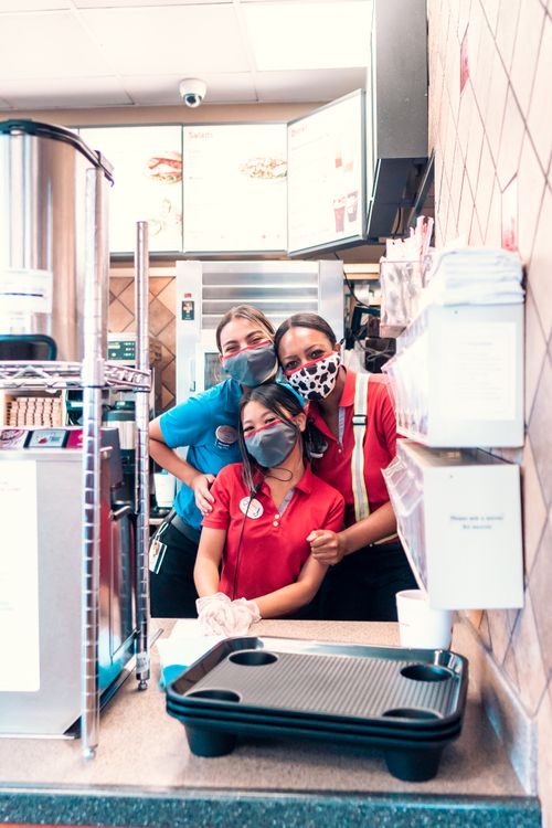 Free Three diverse women in uniforms and face masks posing in a fast-food restaurant. Stock Photo