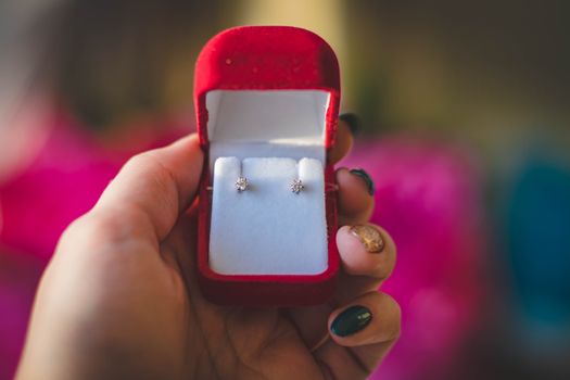 Elegant diamond earrings displayed in a luxurious red velvet box held by a hand.