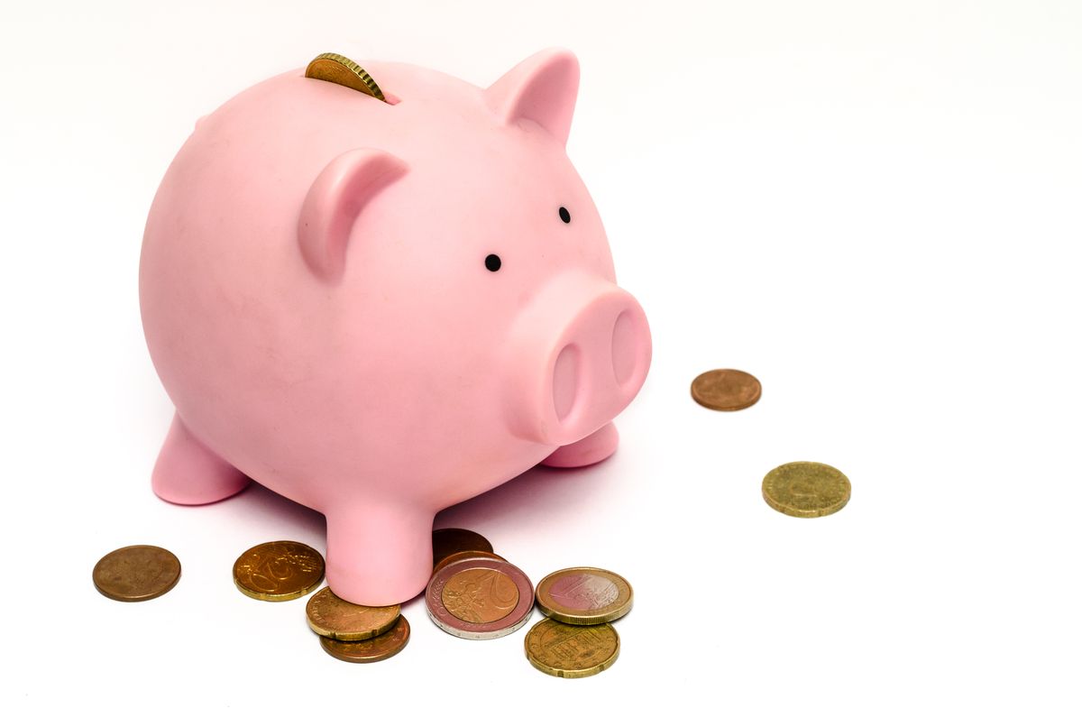 Cofrinho rosa cercado de moedas representando construção de patrimônio e independência financeira