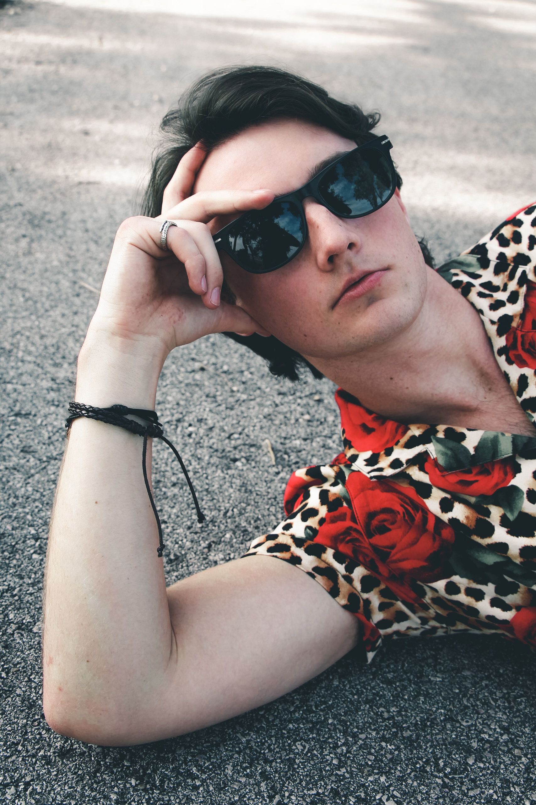 Fashionable man in sunglasses and floral shirt relaxing on the ground in a cool pose.