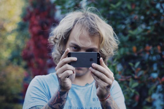 A tattooed man captures a photo with his smartphone against a colorful outdoor backdrop.