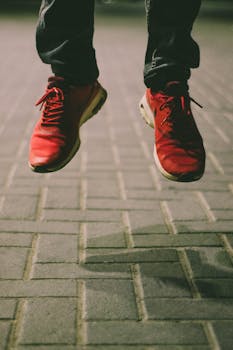 Close-up of red sneakers in mid-jump over a brick pavement, showcasing motion and style.