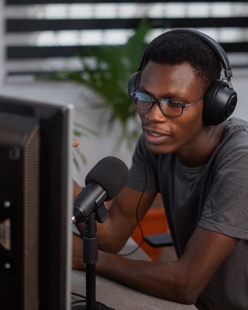 Free A young man wearing headphones and eyeglasses podcasting indoors with a microphone. Stock Photo