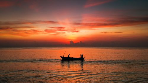 Free Silhouette of a boat on a serene sea during a stunning orange sunrise, creating a tranquil scene. Stock Photo
