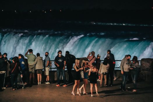 A group of tourists enjoying Niagara Falls at night with illuminated waters.