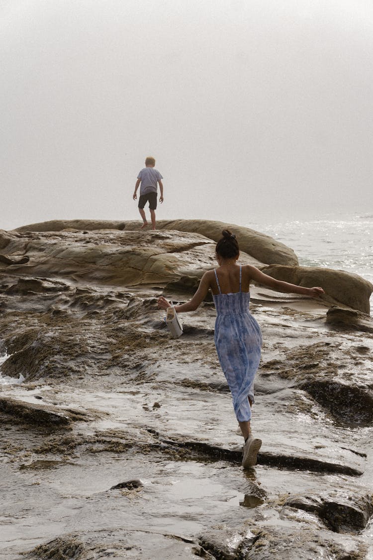 Boy And Girl Playing On Rock Near Body Of Water