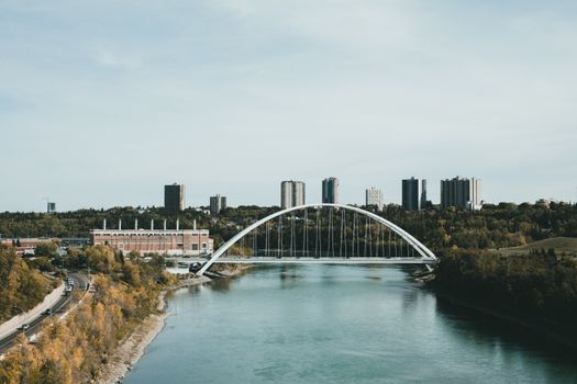 A contemporary cityscape with a modern bridge crossing a calm river, framed by high-rise buildings.