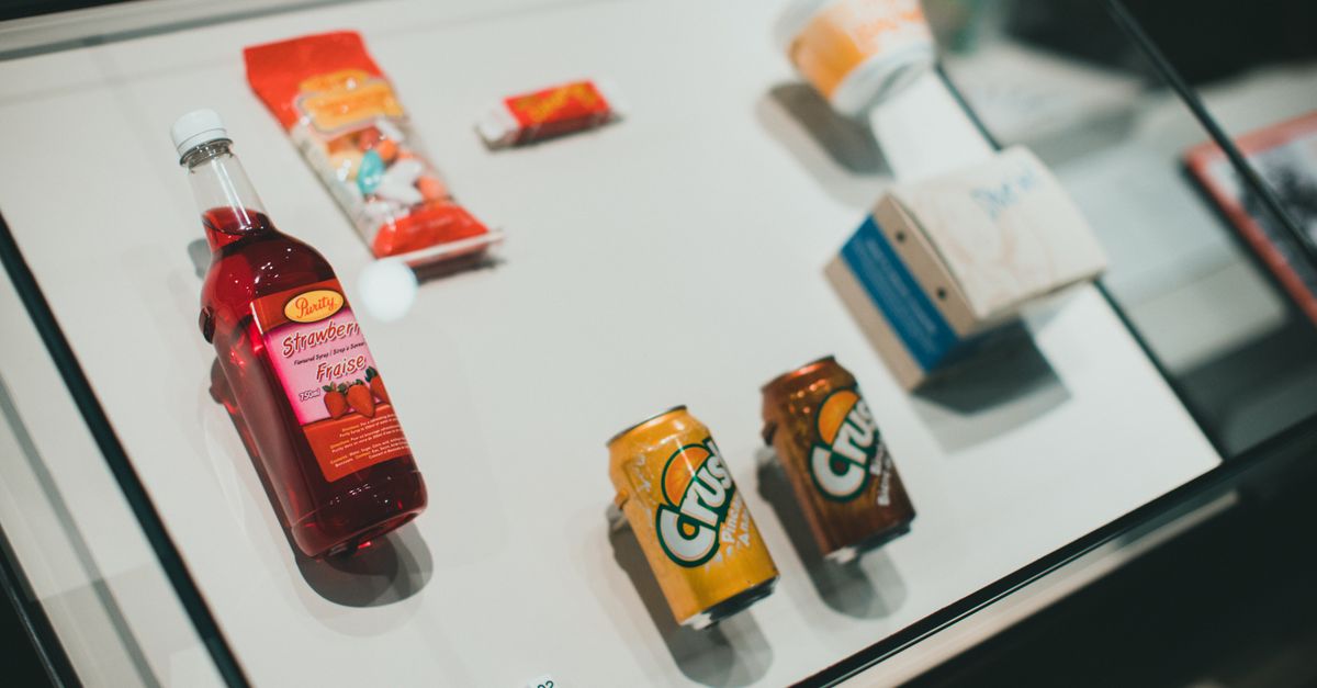 A vibrant, messy soda shop counter with bottles of Torani syrup, cans of Diet Coke, and cups filled with colorful, creamy soda drinks