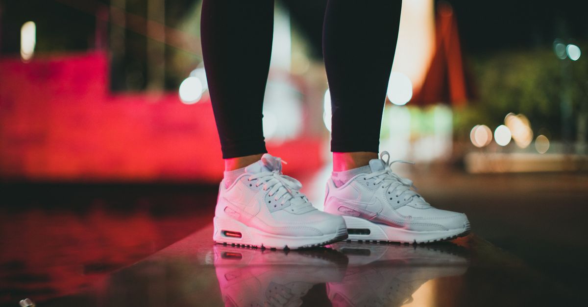 Close-up of trendy white sports sneakers reflecting on a glossy surface with blurred city lights.