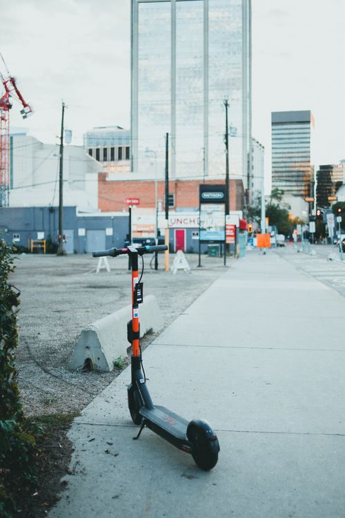 Free A parked electric scooter on a city sidewalk with modern buildings in the background. Stock Photo