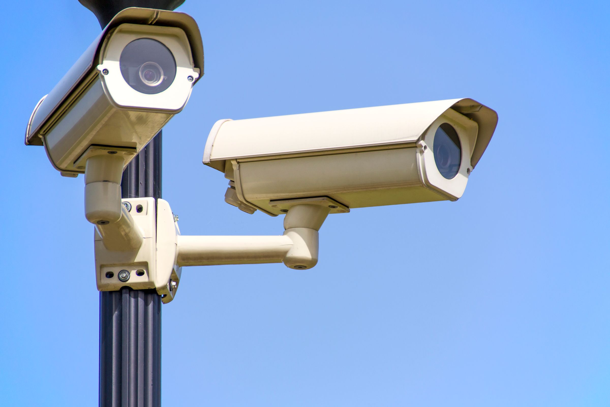 Two surveillance cameras mounted on a pole against an empty sky