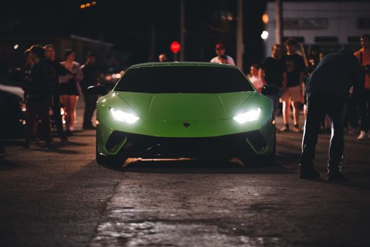 A vibrant green Lamborghini Huracan showcased among a crowd during a night car event.