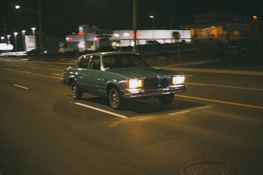 A classic vintage car driving down a dimly lit urban street at night.