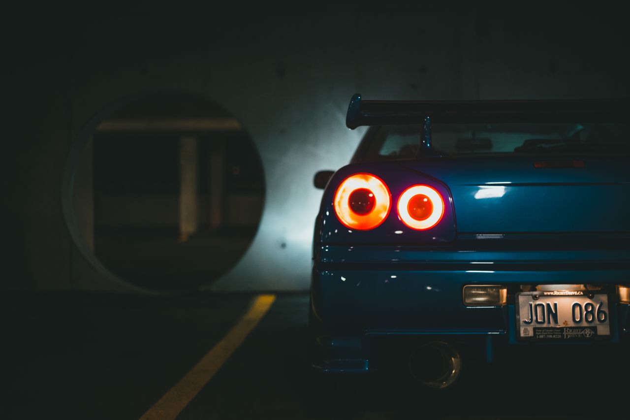 dark rear view of a sleek blue car parked in a low lit parking garage