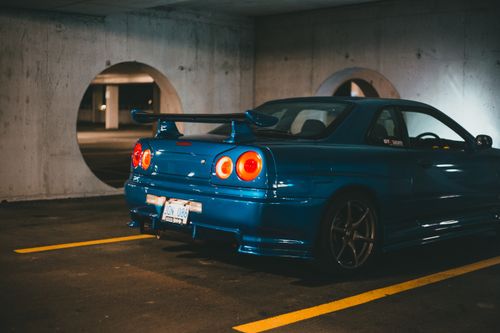 Free Dynamic shot of a blue Nissan Skyline sports car, showcasing its sleek design in a dimly lit parking garage. Stock Photo